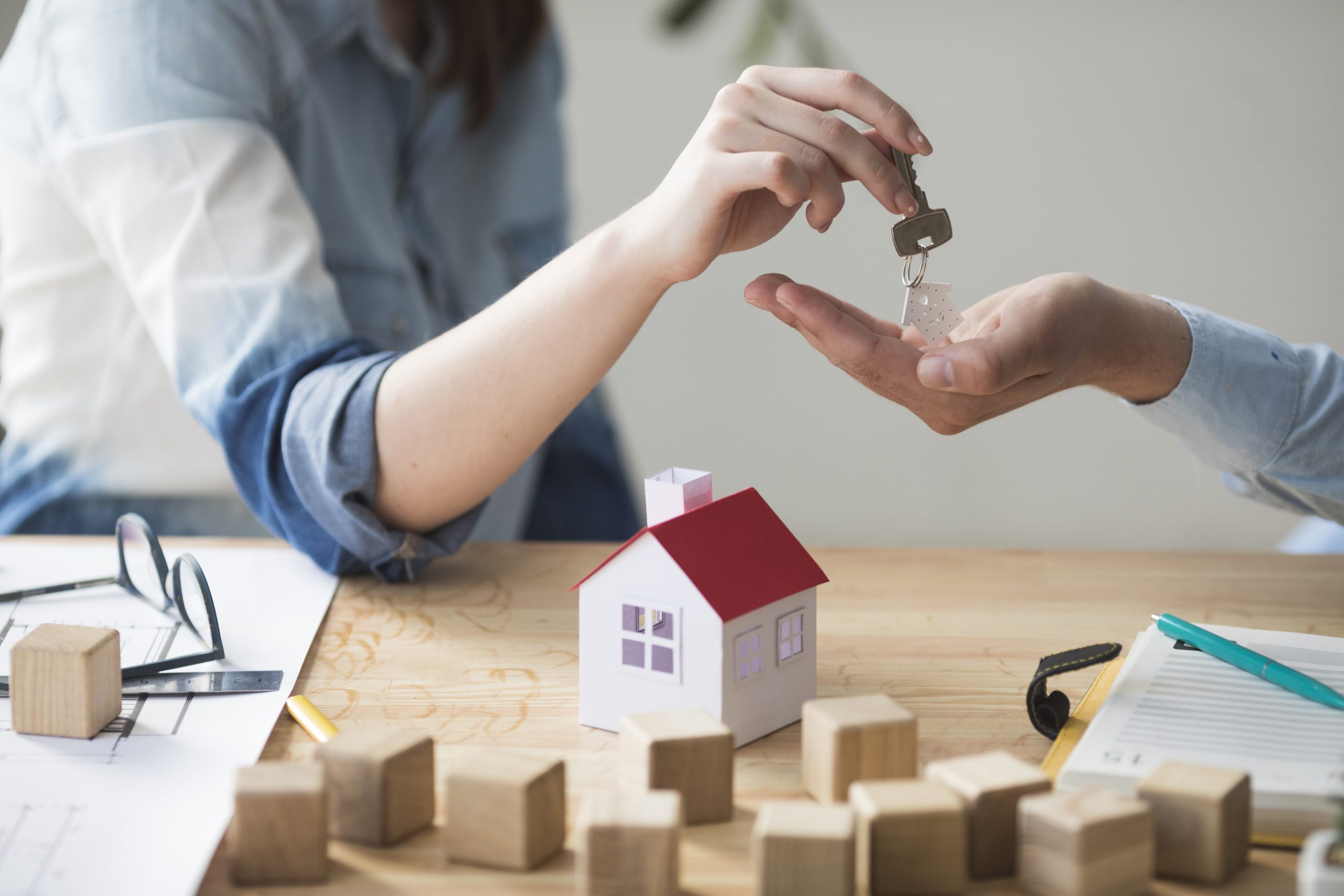 close-up-of-woman-s-hand-giving-house-key-to-man-over-wooden-table